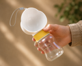 Portable dog water bottle Cuki Flow Mini with cloud-shaped bowl, held indoors with natural light